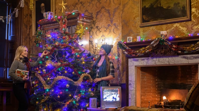 Two women adjusting a Christmas tree in a 1990s lounge setting at Dyrham Park, South Gloucestershire